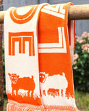 Orange and white towel with sheep design hanging on a wooden rod outdoors.