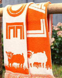 Orange and white towel with sheep design hanging on a wooden rod outdoors.