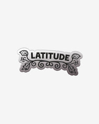 The Pin Badge by 2025 features the word LATITUDE in bold black letters, accented with ornate swirls and leaf designs around the text, set against a white background.
